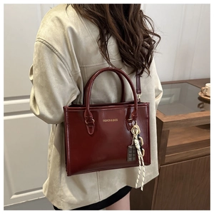 Détail du sac à main bordeaux avec lettrage doré et breloque porté par le mannequin