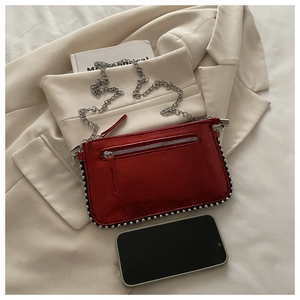 Detail van rode metallic crossbodytas met studs en ketting op een licht pak