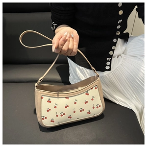 Detailed close-up of a stylish cream underarm bag with vibrant cherry prints and leather trim