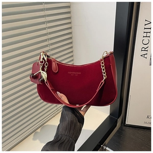 Détail d'un sac demi-lune en velours rouge avec chaîne dorée et pendentif cerise