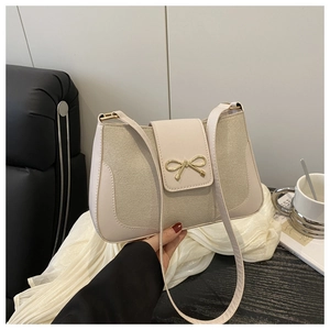 Detail of beige shoulder bag featuring a gold bow ornament on textured fabric