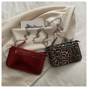 Detail van rood metallic en luipaard crossbodytassen met zilveren ketting en studs