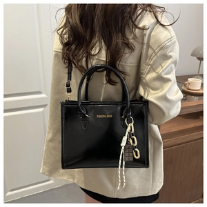 Détail du sac à main noir brillant avec logo doré et pendentifs décoratifs en chaîne