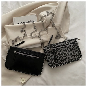 Detail van mini crossbodytassen met zilveren klinknagels en kettingen op een beige blazer