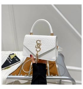 Close-up of white crossbody bag featuring woven texture flap and golden tassel charm