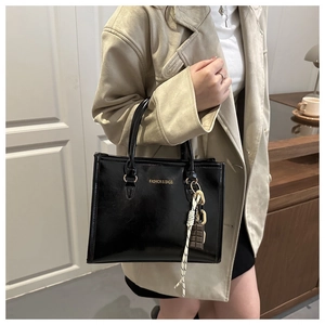 Détail latéral d'un sac à main noir brillant avec lettrage doré et bijou de sac