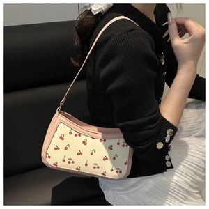 Detail of pink cherry print shoulder bag worn with a black knit cardigan