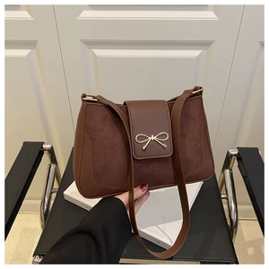 Detail of dark brown faux leather shoulder bag with suede texture and golden bow buckle