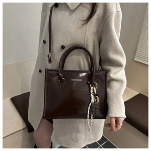 Détail d'un sac cabas marron chocolat brillant avec pendentif cacao et poignées élégantes