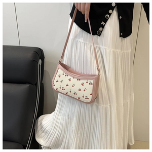 Detail of pink and white shoulder bag with cherry print held by a model in casual outfit