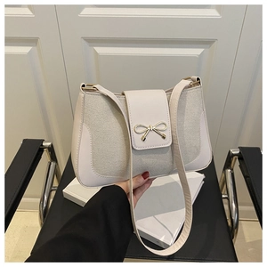 Close-up of cream shoulder bag with golden bow buckle and premium textured fabric