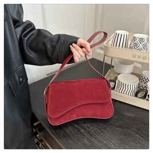 Detail view of burgundy suede handbag showing curved bottom and smooth matte texture
