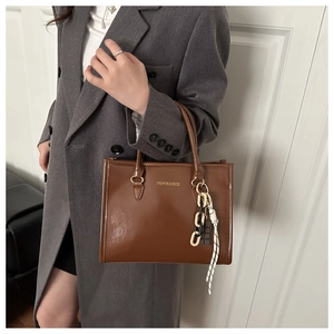 Détail d'un sac cabas en cuir verni marron avec lettrage doré et bijou de sac