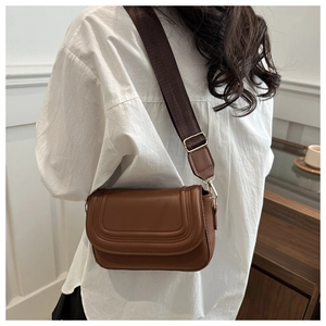 Caramel saddle bag detail with U-shaped stitching and wide textile strap on model