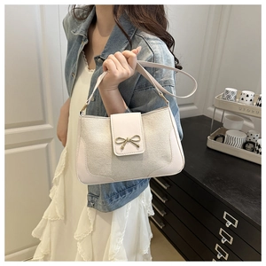 Detail of cream leather shoulder bag with a gold bow buckle shown in a modern home setting