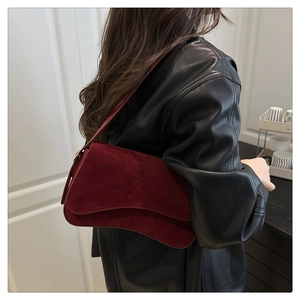 Detail of burgundy suede baguette bag featuring a unique wavy flap and slim shoulder strap