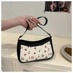 Detail of trendy cherry print baguette bag with black leather trim and metal chain strap