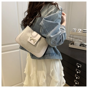 Chic beige shoulder bag with suede texture and gold bow detail shown in lifestyle setting