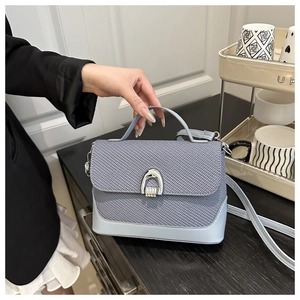 Détail du sac bandoulière bleu clair montrant le tissu tissé et la boucle en métal argenté