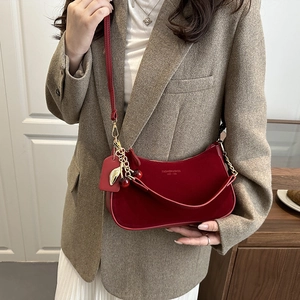 Sac à bandoulière rouge foncé chic avec breloque cerise porté par un mannequin en blazer