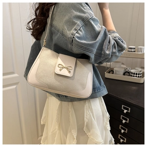 Detail of crossbody bag featuring a golden bow metal buckle on cream leather texture