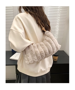 Détail du sac bandoulière matelassé en peluche beige porté par un mannequin en ville