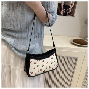 Detail view of cream baguette bag with cherry print and black chain strap styling