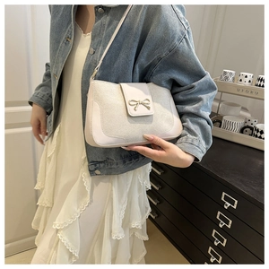 Close-up of cream white shoulder bag featuring a golden metal bow and leather texture