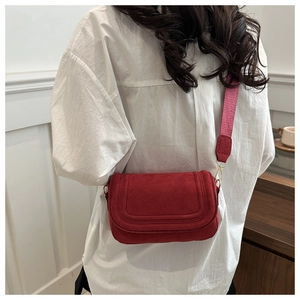 Detail of red suede saddle bag featuring wide woven strap and gold hardware accents