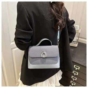 Détail du sac selle bleu clair avec texture tressée et boucle en métal fer à cheval argent