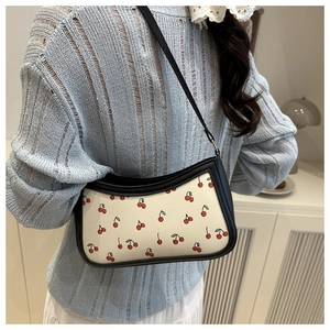 Detail of trendy cherry print underarm bag with black leather strap on female model