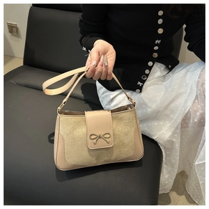Close-up of beige handbag with matte leather texture and golden bow buckle detail