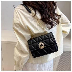 Close-up of black quilted chain strap bag with golden U-shaped lock on a model