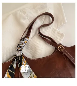 Detail of a brown leather tote bag with a decorative floral silk scarf on the handle