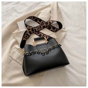 Detail of black leather bucket bag with gold handle and woven geometric shoulder strap