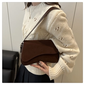 Brown suede underarm bag shown on model wearing beige knit sweater in a cozy setting