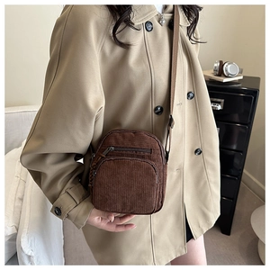Close-up of a coffee brown corduroy crossbody bag worn over a beige trench coat