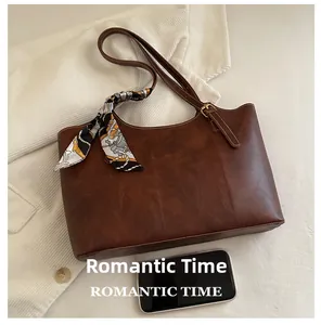 Size comparison of brown leather tote bag with printed scarf against a smartphone