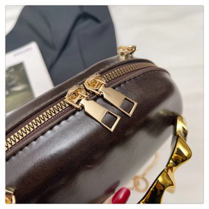 Close-up of luxury dark brown leather handbag featuring gold wave handles and dual zippers