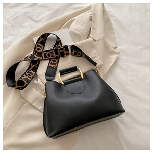 Detail of black bucket bag with a gold semi-circle handle and patterned wide strap