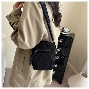 Detail of black corduroy crossbody bag with double zippers and woven pulls on a model