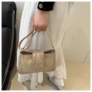 Detail of beige shoulder bag with a gold bow metal clasp and textured suede finish