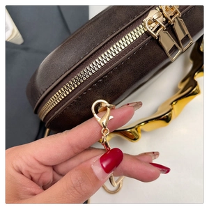Detail of dark brown acrylic evening bag with gold chain strap and wave metal handle