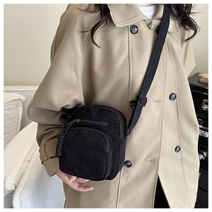 Detail of black corduroy crossbody bag texture and front zipper pocket on model