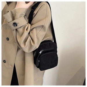 Detail of black corduroy crossbody bag texture and adjustable strap on khaki trench coat