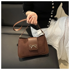Detailed shot of brown suede crossbody bag featuring a golden bow metal decoration