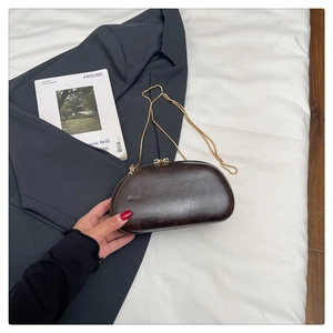 Detailed view of brown semi-circular acrylic clutch bag with a golden chain strap