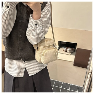Detail of beige corduroy crossbody bag with outer zipper pocket and knit ball charm