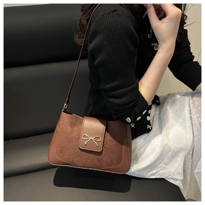 Close-up of brown crossbody bag with metal bow detail worn by a model on a sofa