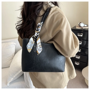 Detail of black matte leather tote bag with contrast stitching and floral silk scarf accessory